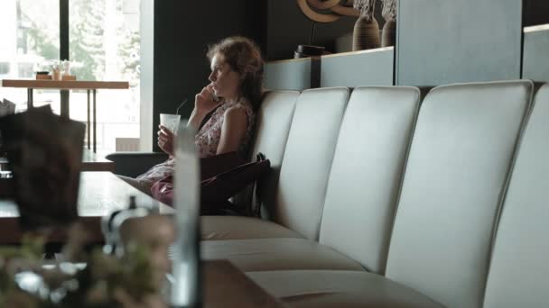 Νεαρή γυναίκα που κάθεται σε ένα τραπέζι σε ένα εστιατόριο. Μετέφερε ένα φορητό υπολογιστή με πρόσβαση στο διαδίκτυο, ελέγχει την αλληλογραφία και πίνοντας καφέ. Μοιάζει πολύ χαρούμενος — Αρχείο Βίντεο