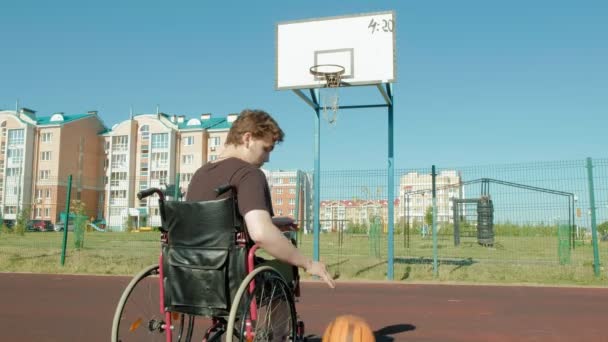 El hombre discapacitado juega baloncesto desde su silla de ruedas, al aire libre — Vídeos de Stock