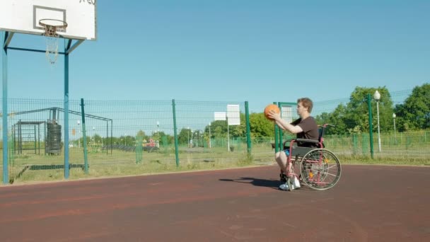 Gehandicapte man speelt basketbal van zijn rolstoel, op de open lucht — Stockvideo