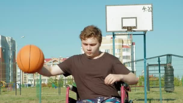 El hombre discapacitado juega baloncesto desde su silla de ruedas, al aire libre — Vídeos de Stock