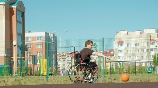 El hombre discapacitado juega baloncesto desde su silla de ruedas, al aire libre — Vídeos de Stock