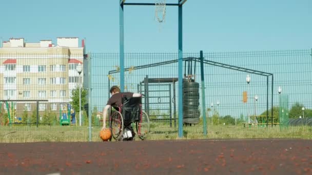 Homem com deficiência joga basquete de sua cadeira de rodas, ao ar livre — Vídeo de Stock