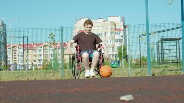 El hombre discapacitado juega baloncesto desde su silla de ruedas, al aire libre — Vídeo de stock