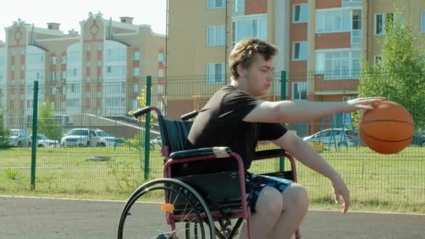 El hombre discapacitado juega baloncesto desde su silla de ruedas, al aire libre — Vídeo de stock