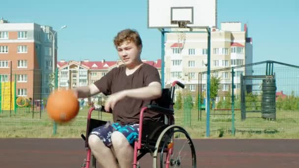 Handikappade mannen spelar basket från sin rullstol, på öppen luft, göra en insats när man spelar — Stockvideo