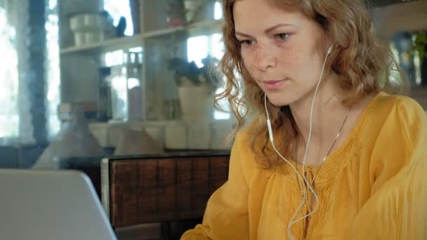 若い女性がカフェに座って現代のラップトップのヘッドフォン — ストック動画