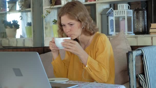 Молодая женщина с современным ноутбуком сидит в кафе и пьет кофе капучино — стоковое видео