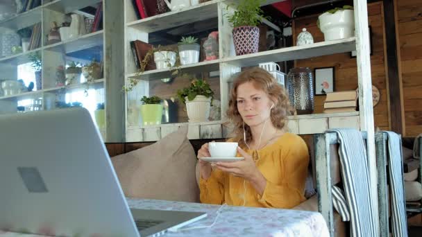 Ung kvinna med en modern laptop sitter på ett café och dricka kaffe cappuccino — Stockvideo