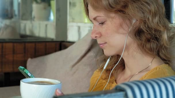 Молода жінка з сучасним ноутбуком сидить в кафе і п'є каву капучино — стокове відео