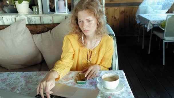 Fiatal nő ül egy kávézóban, és cappuccino kávét iszik, egy korszerű laptop — Stock videók