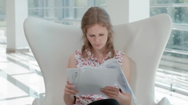 Attractive businesswoman sitting on a white chair in a glass office and checks documents — Stock Video