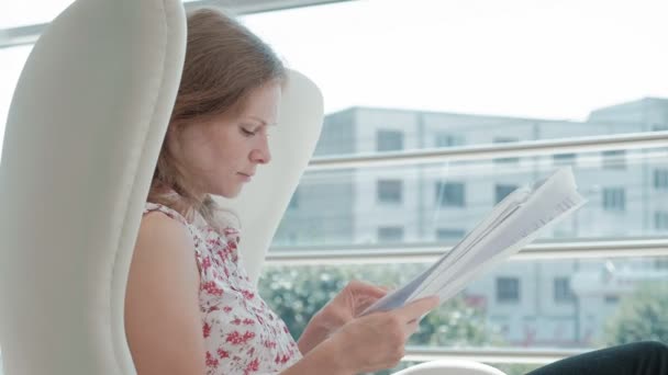 Приваблива бізнес-леді сидить на білому стільці в скляному офісі і перевіряє документи — стокове відео