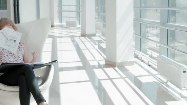 Jolie femme d'affaires assise sur une chaise blanche dans un bureau en verre et vérifie les documents — Video