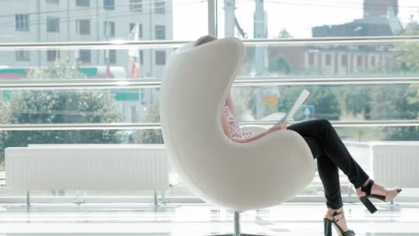 Ελκυστικός επιχειρηματίας που κάθεται σε μια λευκή καρέκλα σε ένα γυάλινο γραφείο και ελέγχους έγγραφα — Αρχείο Βίντεο