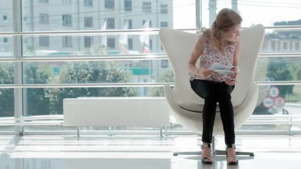 Attractive businesswoman sitting on a white chair in a glass office and checks documents — Stock Video