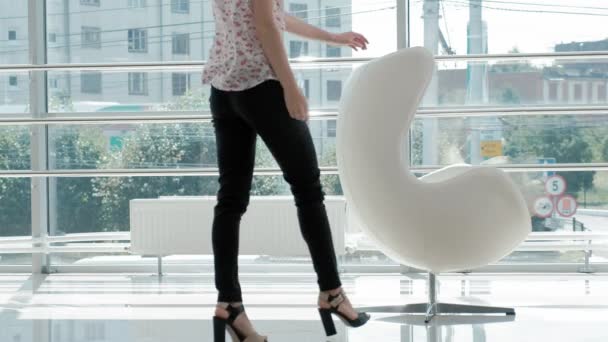 Attraktive Geschäftsfrau sitzt auf einem weißen Stuhl in einem gläsernen Büro und prüft Dokumente — Stockvideo