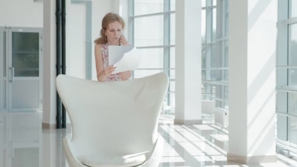 Attractive businessman sitting on a white chair in a glass office and checks documents — Stock Video