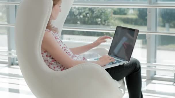 Atractiva mujer de negocios sentada en silla blanca en la oficina de cristal y trabajando detrás de la computadora portátil — Vídeo de stock