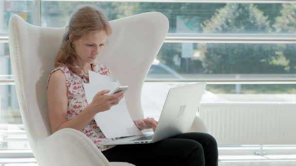 Attraktive Geschäftsfrau sitzt auf weißem Stuhl im gläsernen Büro und arbeitet hinter Laptop — Stockvideo