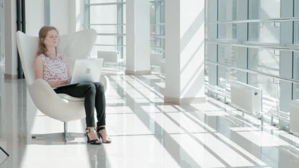 漂亮的女商人坐在玻璃办公室的白色椅子上, 工作在笔记本电脑后面 — 图库视频影像