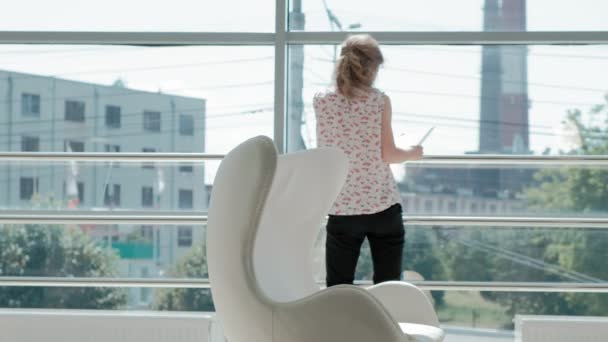 Attractive businessman sitting on a white chair in a glass office and checks documents — Stock Video