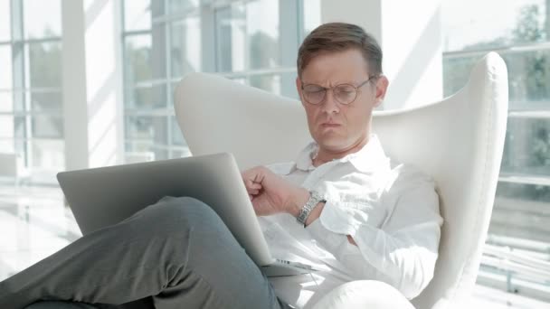 Homem de negócios atraente sentado em uma cadeira branca em um escritório de vidro e verifica documentos — Vídeo de Stock