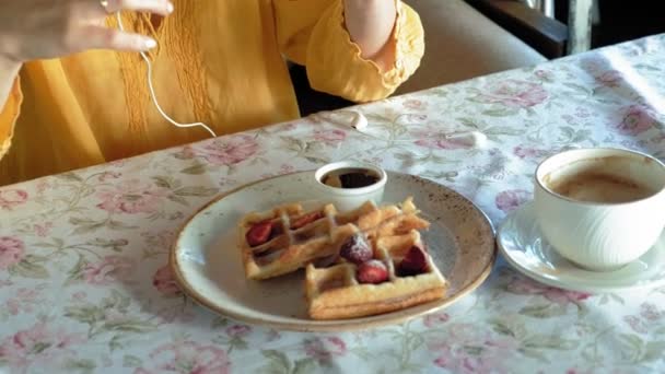 Mooie vrouw is het eten van wafels in café gebruikt een smartphone om een foto te maken — Stockvideo