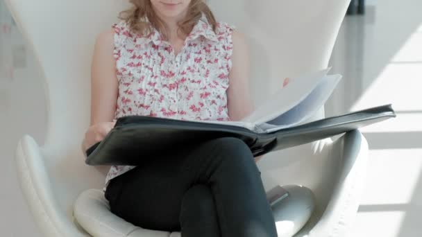 Jolie femme d'affaires assise sur une chaise blanche dans un bureau en verre et vérifie les documents — Video