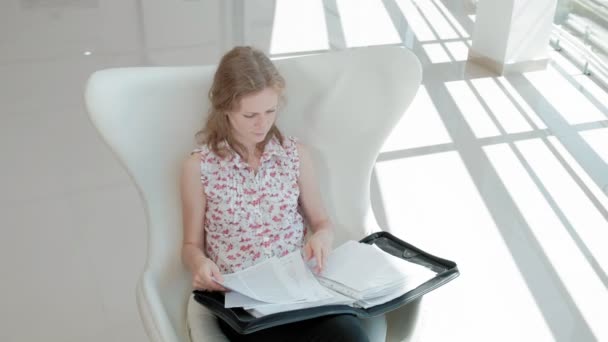 Jolie femme d'affaires assise sur une chaise blanche dans un bureau en verre et vérifie les documents — Video