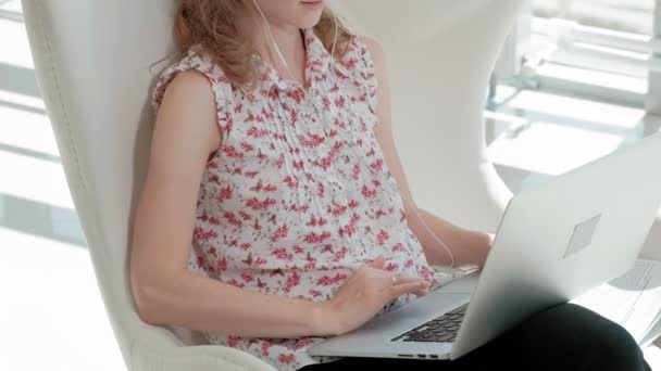 Привлекательная деловая женщина сидит на белом стуле в стеклянном офисе и работает за ноутбуком — стоковое видео