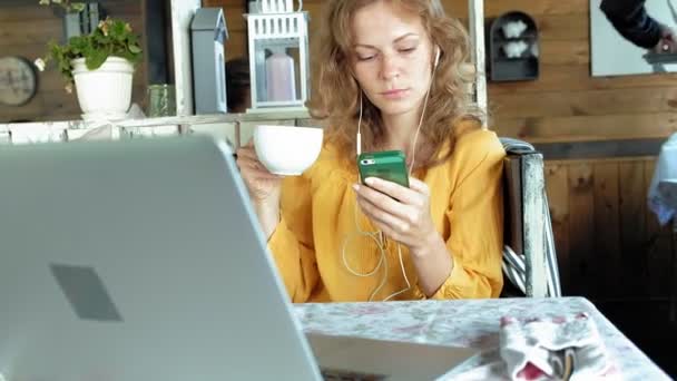 Jeune femme avec un ordinateur portable moderne assis dans un café et boire du café cappuccino — Video