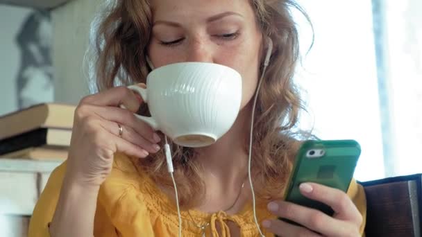 Fiatal nő ül egy kávézóban, és cappuccino kávét iszik, egy korszerű laptop — Stock videók