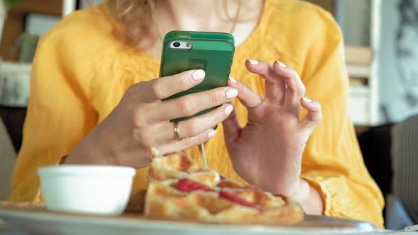 Beautiful woman is eating waffles in cafe uses a smartphone to take a photo — Stock Video