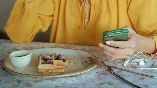 Hermosa mujer está comiendo gofres en la cafetería utiliza un teléfono inteligente para tomar una foto — Vídeo de stock