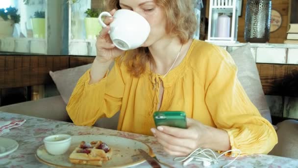 Gyönyörű nő eszik gofri café használja a smartphone-hoz fog egy fénykép — Stock videók