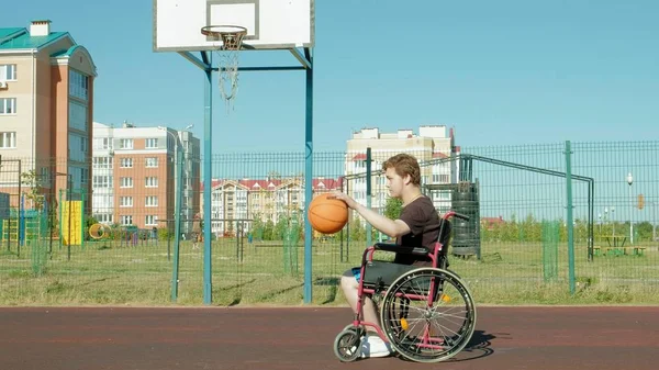 Homem com deficiência joga basquete de sua cadeira de rodas, ao ar livre — Fotografia de Stock