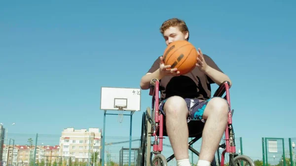 Homem com deficiência joga basquete de sua cadeira de rodas, ao ar livre — Fotografia de Stock