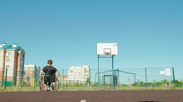 Homem com deficiência joga basquete de sua cadeira de rodas, ao ar livre — Fotografia de Stock