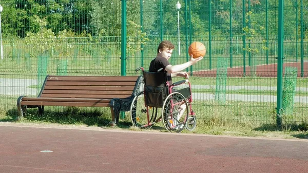 Homem com deficiência joga basquete de sua cadeira de rodas, ao ar livre — Fotografia de Stock