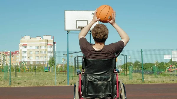 Homem com deficiência joga basquete de sua cadeira de rodas, ao ar livre — Fotografia de Stock