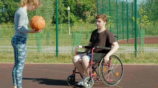 Homem com deficiência joga basquete de sua cadeira de rodas com uma mulher, ao ar livre, fazer um esforço ao jogar — Fotografia de Stock