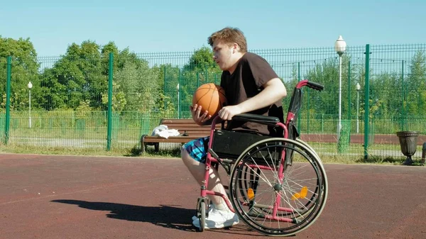 Behinderter spielt Basketball vom Rollstuhl aus, im Freien, gibt sich beim Spielen Mühe — Stockfoto