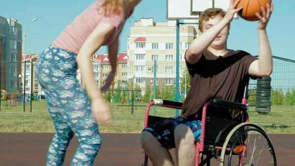 Behinderter spielt Basketball aus seinem Rollstuhl mit einer Frau, an der frischen Luft, bemühen sich beim Spielen — Stockfoto