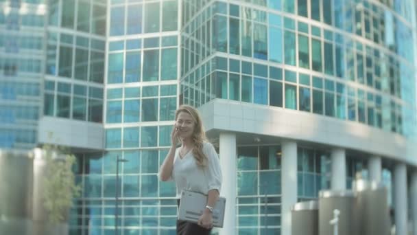 Joven mujer de negocios hablando está utilizando el teléfono inteligente en el centro de negocios del parque de la ciudad — Vídeos de Stock