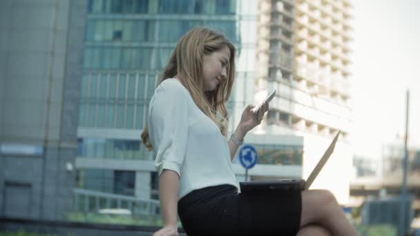 Joven mujer de negocios hablando está utilizando el teléfono inteligente en el centro de negocios del parque de la ciudad — Vídeos de Stock