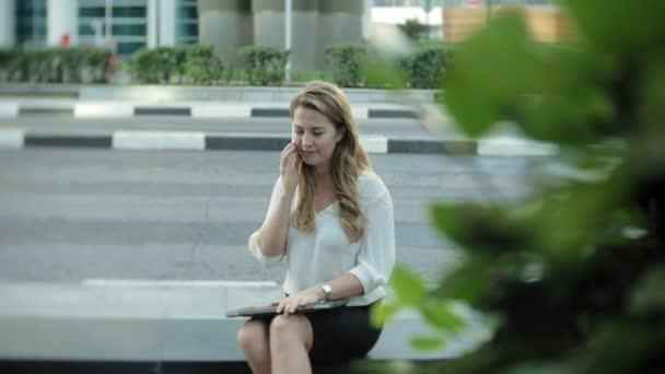 Young businesswoman talking is using smartphone in city park business center — Stock Video