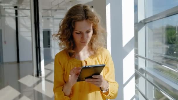 Junge schöne Geschäftsfrau, am Fenster mit einem Tablet — Stockvideo