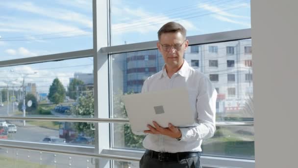 Mature businessman and businesswoman at a window with a laptop — Stock Video