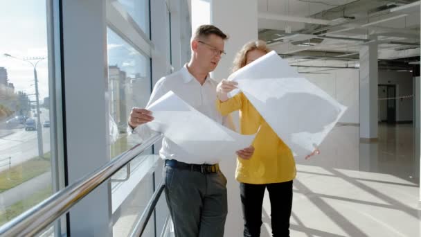 Jonge mooie zakenvrouw en volwassen man, door het raam met een scans een tekening op papier — Stockvideo