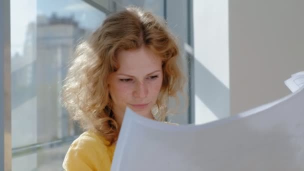 Genç güzel iş kadını, bir çizim kağıt üzerinde inceden inceye gözden geçirmek ile pencere tarafından — Stok video